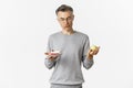 Portrait of thoughtful middle-aged man in glasses, making decision between tasty cake and green apple, standing over Royalty Free Stock Photo