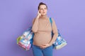 Portrait of thoughtful pregnant woman, trying to remember she takes everything to hospital, keeps finger on temple, looking up