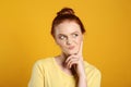 Portrait of thoughtful red haired woman on yellow background