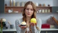 Smiling woman looking at cake and apple in kitchen. Girl preferring fresh fruit.