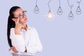 Portrait of a thoughtful young business woman with glasses looking at a light bulb as an Idea. Copy space Royalty Free Stock Photo