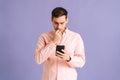 Portrait of thoughtful young man holding phone with doubtful and skeptical expression on pink isolated background. Royalty Free Stock Photo
