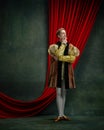 Portrait of thoughtful young man, prince, royal person in retro costume standing against dark green, vintage background