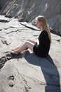 Portrait of young girl in black dress with long blonde hair sitting on beach Royalty Free Stock Photo