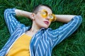 Portrait of thoughtful young woman with short hair in casual blue striped suit, yellow shirt, glasses lying down on green grass, Royalty Free Stock Photo