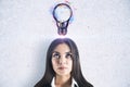 Portrait of thougtful young european businesswoman with creative light bulb sketch on concrete wall background. Idea and