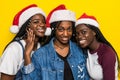 Portrait of three young african women with santa hat hugs isolated on yellow background Royalty Free Stock Photo