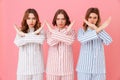 Portrait of three beautiful young girls 20s wearing colorful striped pyjamas showing crossed hands no gesture meaning deny