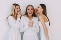 Portrait of three cheerful women standing together and talking secrets in girl& x27;s ears isolated over white background