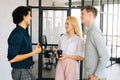 Portrait of three cheerful young colleagues standing in modern loft office talking and discussing business issues during Royalty Free Stock Photo