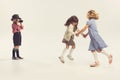 Portrait of three children, little boy taking photo of two cheerful girls holding hands and whirling isolated over grey Royalty Free Stock Photo