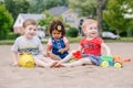 Three cute Caucasian and hispanic latin toddlers babies children sitting in sandbox playing with plastic colorful toys Royalty Free Stock Photo