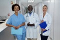 Portrait of three diverse male and female doctors standing in hospital corridor smiling to camera Royalty Free Stock Photo