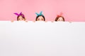 Portrait of three funny people hiding behind pure pattern wearing bright headbands isolated over pink background