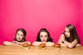 Three sad girls on diet looking at burgers on table.