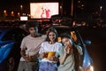 Portrait of three happy young friends smiling at camera while standing together by the car parked in front of a big Royalty Free Stock Photo