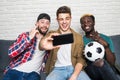 Portrait of three happy young men taking a selfie on phone while sitting at home with beer and snacks Royalty Free Stock Photo