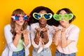 Portrait of three ladies diversity wear big heart star shape sunglass blow confetti isolated on yellow color background