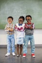 Portrait of three school kids standing with arms crossed against chalkboard