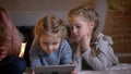 Portrait of three small caucasian girls lying on the floor and watching into tablet with attentiveness in cosy home