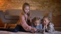 Portrait of three small caucasian girls sitting on the floor and watching into tablet with attentiveness and interest in