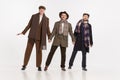 Portrait of three stylish men in warm coats, scarves and hats posing over grey studio background. Male fashion