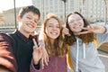Portrait of three teen friends boy and two girls smiling and taking a selfie outdoors. City background, golden hour Royalty Free Stock Photo