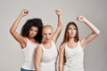 Portrait of three young diverse women wearing white shirts having confident look while showing, raising clenched fist