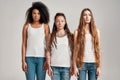 Portrait of three young diverse women wearing white shirts looking at camera while posing together  over grey Royalty Free Stock Photo