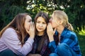 Portrait of three young girlfriends who whisper in the park. Exchange of news, emotional women whispering gossip