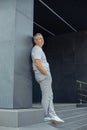 Portrait of tired aged gray haired businessman leaning back on gray construction of modern office building near entrance