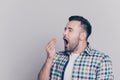 Portrait of tired, bored, attractive man in checkered shirt, closing his open mouth, he wants to sleep, yawning over grey Royalty Free Stock Photo