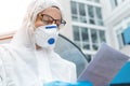 Portrait of tired exhausted female doctor, scientist or nurse wearing face mask and biological hazmat ppe suit reading Royalty Free Stock Photo