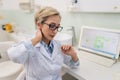 Portrait of tired middle-aged female doctor in eyeglasses having neck pain during working on laptop, suffering from Royalty Free Stock Photo