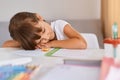 Portrait of tired sleepy child girl with dark hair doing homework being tired of long hours learning, sleeping on table on her Royalty Free Stock Photo