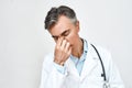 Portrait of tired stressed male doctor in medical uniform feeling upset, keeping eyes closed and touching nose while Royalty Free Stock Photo