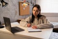 Portrait of a tired student learning online with laptop taking notes in a notebook sitting at her desk at home, looking Royalty Free Stock Photo
