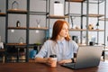 Portrait of tired thinking young business woman sitting at desk with laptop in modern office room, holding cup with Royalty Free Stock Photo