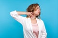 Portrait of tired woman suffering neck ache, standing with closed eyes and massaging neck to relieve pain. blue background Royalty Free Stock Photo