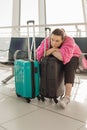 Portrait of tired woman wearing black clothes, pink cardigan, leaning on black suitcase, putting head on folded hands. Royalty Free Stock Photo