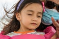 A portrait of toddler girl closing eyes feeling the wind while father in the background wearing face mask on the boat