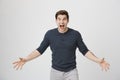 Portrait of too excited young european man, spreading arms and shouting with widen eyes at camera, standing over gray