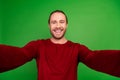 Portrait of toothy beaming handsome guy with long hairstyle wear red sweatshirt smile on selfie isolated on green color Royalty Free Stock Photo