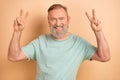 Portrait of toothy beaming senior man with gray beard wear stylish t-shirt two hands showing v-sign isolated on pastel