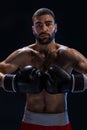 Portrait of tough male boxer posing in boxing stance against black background.