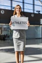 Portrait of tour operator standing while holding white board with ATHLETES signage in arrival area at airport Royalty Free Stock Photo