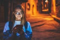 Portrait tourist girl using mobile phone with eyeglasses reflection of screen light backdrop of street old historical city at nigh