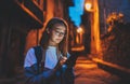 Portrait tourist girl using mobile phone with eyeglasses reflection of screen light backdrop of street old historical city