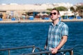 Portrait of tourist and traveler is posing and walking on beach pier, enjoys in sun and view of sea landscape. Man with sunglasses