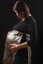 Portrait of Tranquil Pregnant caucasian Woman in Supporting Dress. Against Black Background